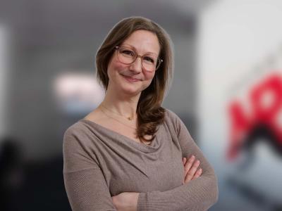 Frau mit braunen Haaren in einem sandfarbenen Oberteil